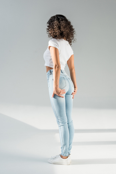 back view of woman standing in tight blue jeans on grey background - Foto, Imagem