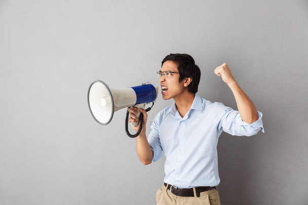 Angry asian business man standing isolated over gray background, screaming at a loudspeaker - Photo, image