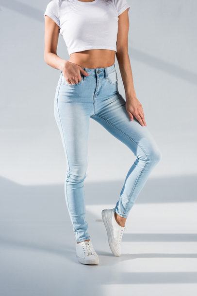 Cropped view of sexy girl in blue jeans standing with hand in pocket on grey background - Foto, Imagem