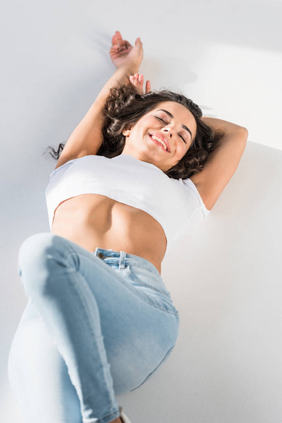Сексуальная улыбающаяся девушка в джинсах, лежащая на светлой поверхности
 - Фото, изображение