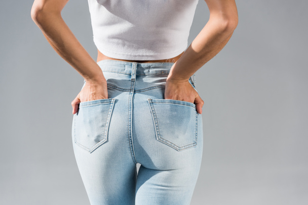 Vista cortada de mulher jovem em jeans com as mãos em bolsos isolados em cinza
  - Foto, Imagem