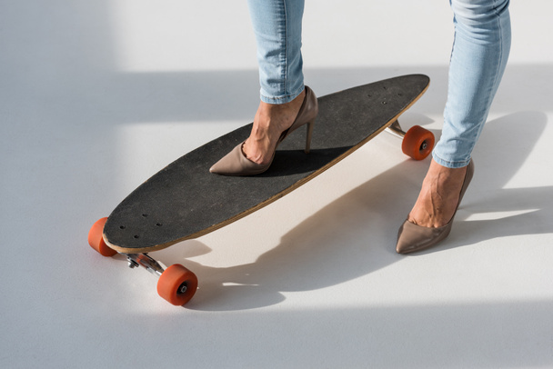Cropped view of woman in high-heeled shoes standing on longboard - Fotografie, Obrázek
