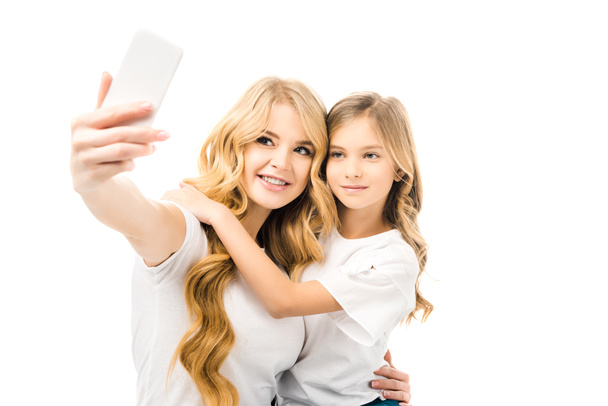 smiling mother taking selfie while embracing adorable daughter isolated on white - Photo, Image