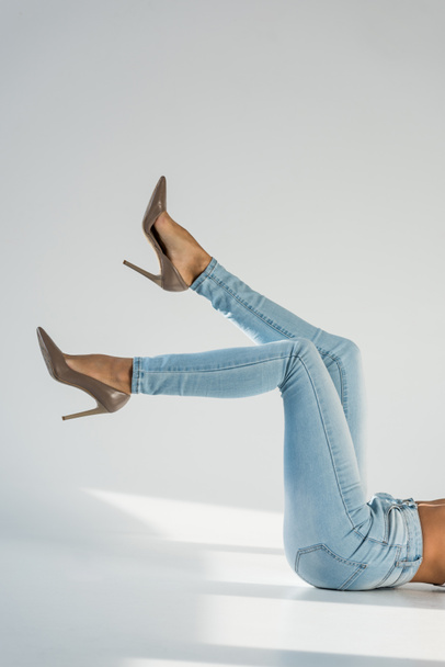 Partial view of woman in blue jeans and high-heeled shoes on grey background - Foto, Imagem