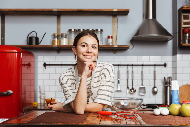 Happy young woman standing at the kitchen at home - Photo, image