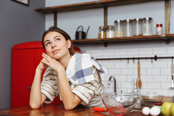 Happy young woman standing at the kitchen at home - Foto, Bild
