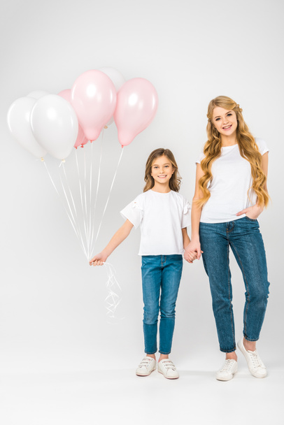 cheerful child with festive air balloons holding hands with smiling mother on white background - Photo, Image