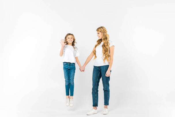 happy daughter jumping and waving hand while holding mothers hand on white background - 写真・画像
