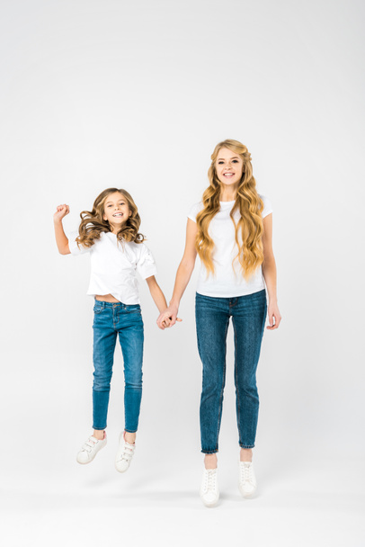 carefree child jumping while holding mothers hand on white background - Foto, immagini