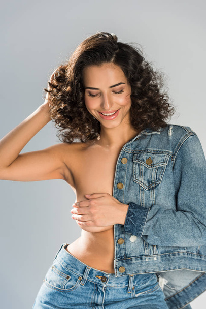 Laughing topless girl in jeans touching hair isolated on grey  - Zdjęcie, obraz