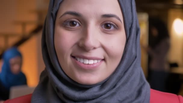 Closeup portrait of young beautiful arabian female face in gray hijab looking straight at camera with pretty brown eyes and smiling facial expression - Filmati, video