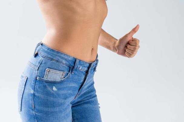 Cropped view of woman in jeans showing thumb up on grey background - Fotoğraf, Görsel