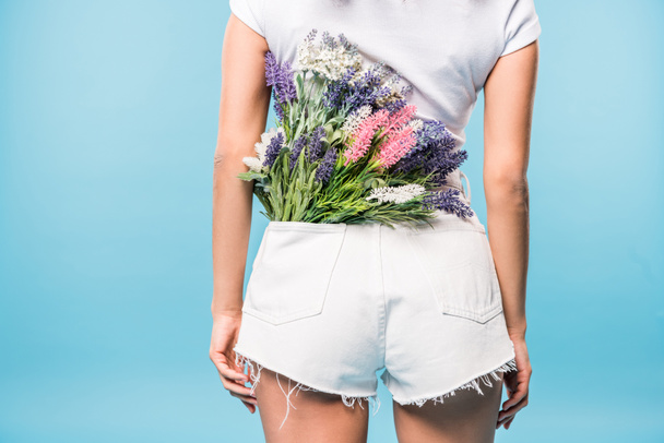 Cropped view of woman in shorts with flower bouquet in pocket on blue background - Foto, Bild