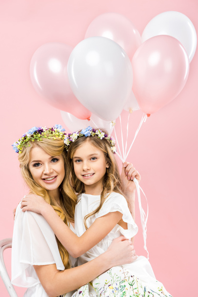 Gelukkig moeder zitten met schattige dochter ingedrukt te lucht ballonnen op roze achtergrond - Foto, afbeelding