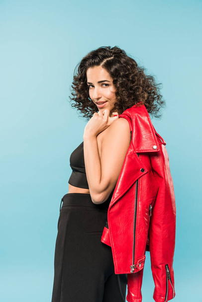 Graceful curly girl holding red leather jacket on blue background - Foto, afbeelding