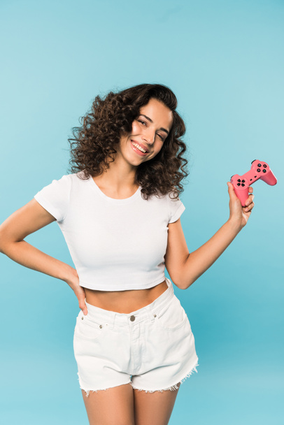Slim laughing woman in shorts holding gamepad on blue background - Photo, Image