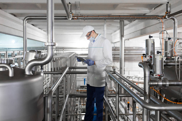 Τεχνολόγος στέκεται με ένα tablet στο κατάστημα στο εργοστάσιο γαλακτοκομικών προϊόντων - Φωτογραφία, εικόνα
