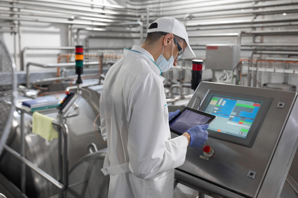 Technologist stands with a tablet near the digital screen at the dairy Plant - Photo, Image