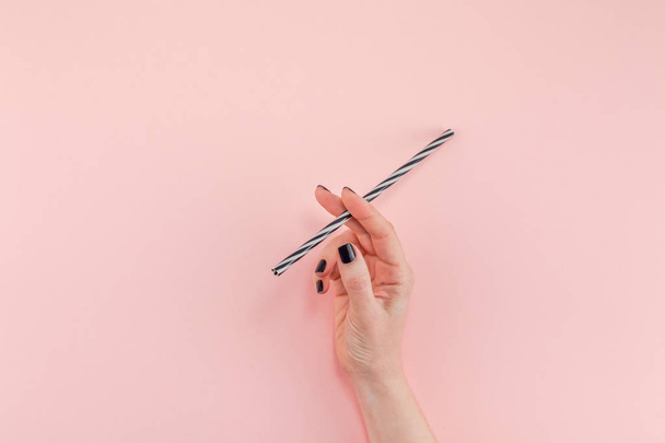 Creative top view flat lay of woman hand with black manicure holding cocktail drinking straw like cigarette with copy space pink paper background minimalism style. Template feminine blog social media - Photo, Image