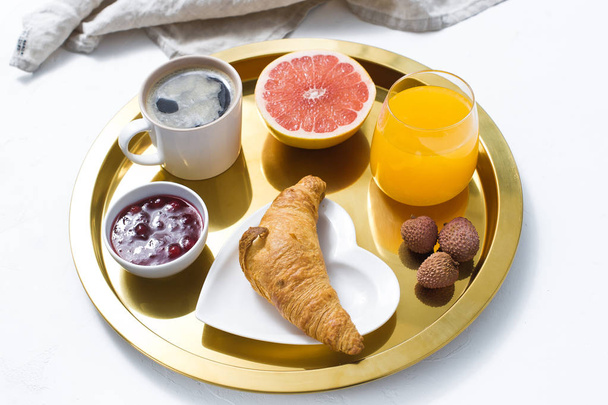 French Breakfast on a Golden tray, coffee, jam, croissant, orange juice, grapefruit, lychee. Top view, white background - Foto, Imagen