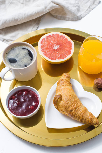 Desayuno francés en bandeja dorada, café, mermelada, croissant, zumo de naranja, pomelo, lichi. Vista superior, fondo blanco
 - Foto, imagen