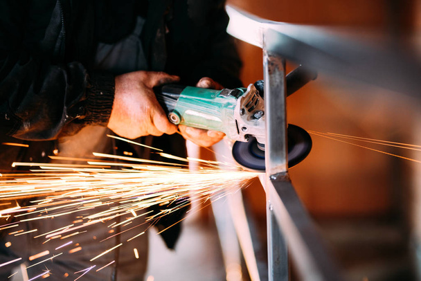 Heavy industry worker cutting steel with angle grinder on construction site - 写真・画像