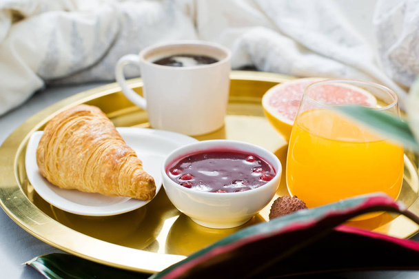 Desayuno en la cama, servicio de hotel. Café, mermelada, croissant, zumo de naranja, pomelo, lichi. Vista lateral, fondo claro
 - Foto, imagen