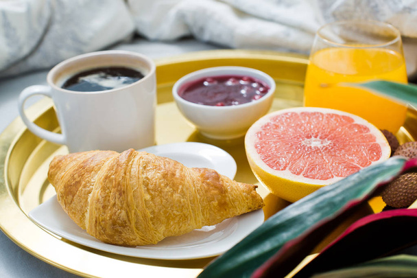 Κλασικό γαλλικό πρωινό στο κρεβάτι, ξενοδοχείο υπηρεσία. Καφέ, μαρμελάδες, κρουασάν, χυμό πορτοκάλι, γκρέιπφρουτ, λίτσι. Πλάγια όψη, ανοιχτόχρωμο φόντο - Φωτογραφία, εικόνα