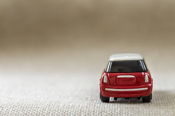 ライト ベージュのキャンバス布コピー スペース背景に暗い窓のある小さな明るい赤い金属単純な子供のおもちゃの車. - 写真・画像