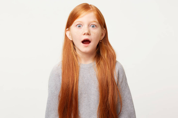 Red-haired girl in shock, nervous frozen in place, stands with her mouth wide open and bulging blue eyes in fear. The child saw something forbidden unexpected scary. - Foto, imagen