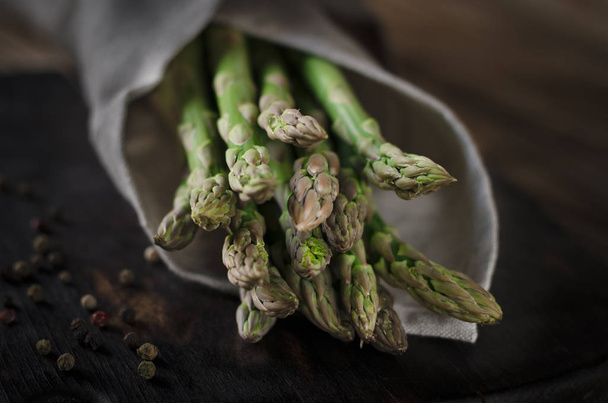Green juicy asparagus is lying on a wooden dark board on a brown wooden table. - Фото, зображення