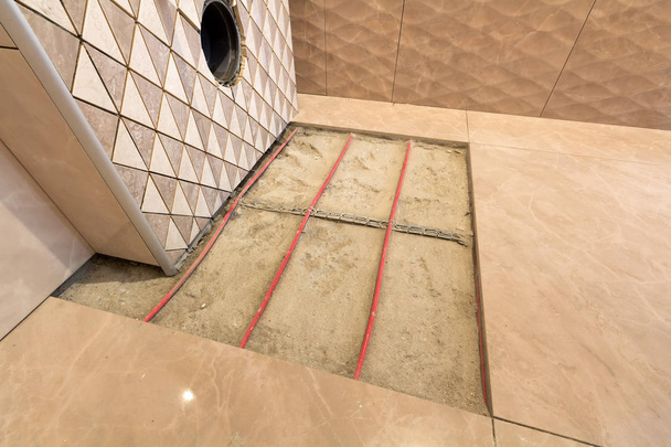 Незакінчена реконструкція ванної кімнати з керамічною плиткою, встановленою на стінах, нагрівання системи електричних кабелів на цементній підлозі та місце для туалету
. - Фото, зображення
