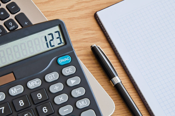 Калькулятор с блокнотом и шариковой ручкой на деревянном столе
 - Фото, изображение