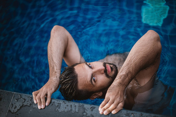 Portrét pohledný mladík ve venkovním bazénu. Atraktivní chlapík s plnovousem na straně fondu - Fotografie, Obrázek