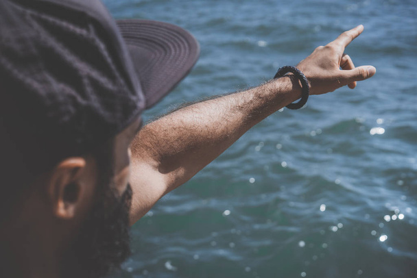 Muotokuva Huomaavainen parrakas mies osoittaa miehen käsi meren rannalla ja katselee kaukaisuuteen horisontissa meressä. lähikuva-analyysi
. - Valokuva, kuva