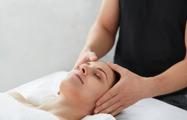 Young beautiful woman enjoying anti-aging facial massage.Male therapist making head massage to female client.Professional masseur.Relaxation,beauty,spa,body and face treatment concept.  - Фото, зображення