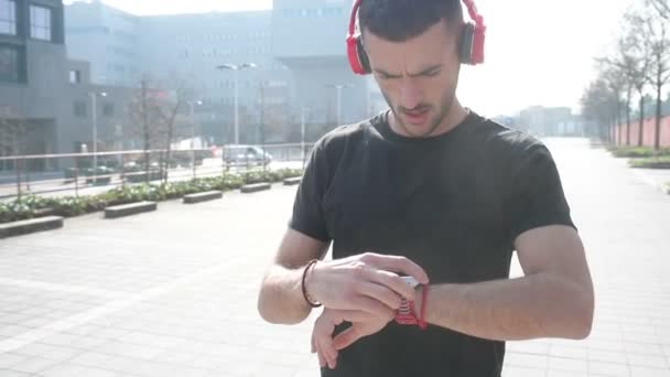 νεαρός άνδρας υπαίθρια χρησιμοποιώντας SmartWatch ακούει μουσική ασύρματη τεχνολογία, μουσική, έννοια του αθλητισμού - Πλάνα, βίντεο