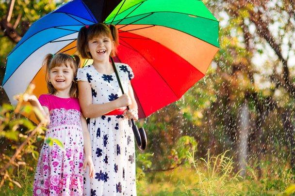 Дети с красочным зонтиком играют в осенний дождь в душе. Маленькие девочки играют в парке в дождливую погоду. Осенние развлечения на открытом воздухе для детей
. - Фото, изображение