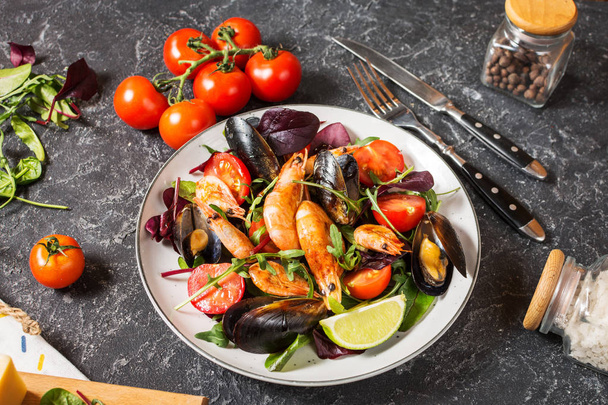 Fresh seafood salad, mussels, shrimp, fresh vegetables and herbs on black stone background - Photo, Image