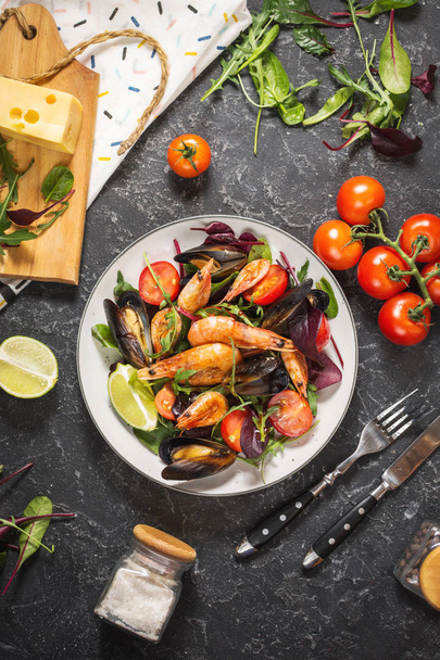 Salade van verse visgerechten, mosselen, garnalen, verse groenten en kruiden op zwarte stenen achtergrond. Bovenaanzicht - Foto, afbeelding