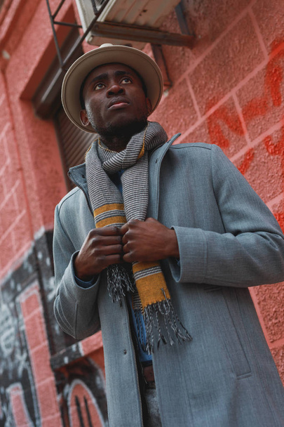 Street portrait of african american man in coat and hat at the red building background - Foto, afbeelding