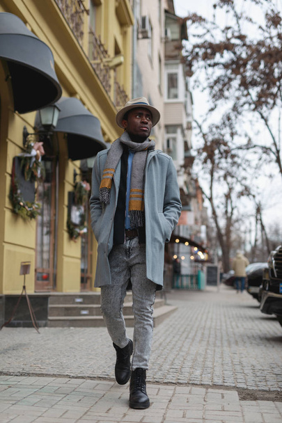 Fashion model african american man in coat and hat walking along city street - Photo, image