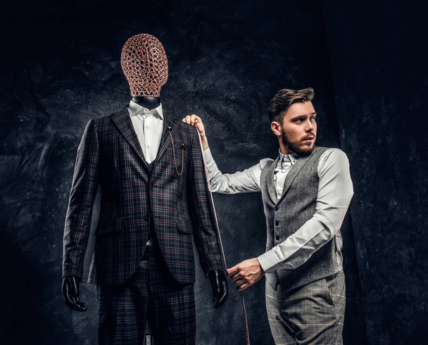 Een modeontwerper met een meetlint controleren de lengte van de mouwen van een aangepaste gemaakte elegante mens pak in een donkere kleermaker studio - Foto, afbeelding