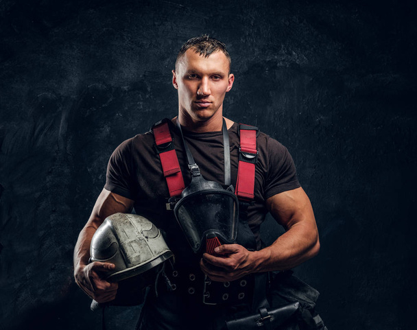 Brutale brandweerman kijkt naar de camera en een helm in zijn hand houdt  - Foto, afbeelding