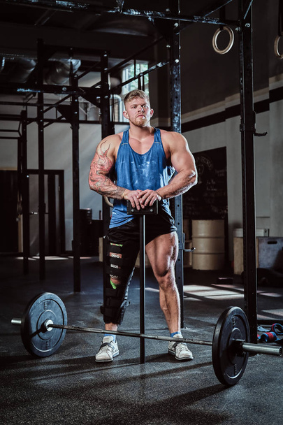 powerlifter professionnel avec un bandage sur une jambe, tenant un marteau de sport, échauffement avant entraînement, récupération des blessures
. - Photo, image