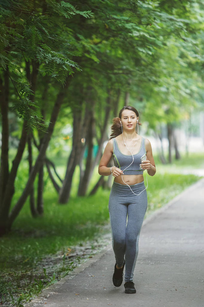 Young woman jogging down path in green park - Valokuva, kuva