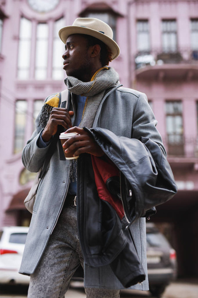 Fashion model african american man in coat and hat walking along city street - Foto, Imagen