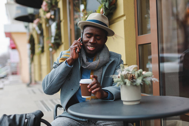 Gelukkig Afro-Amerikaanse man praten met vriend door de smartphone zit op terras - Foto, afbeelding