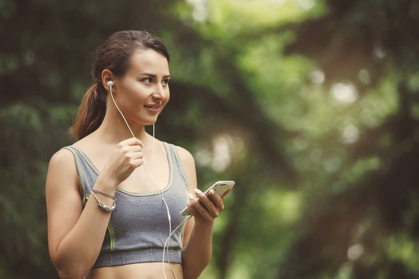 Cute Young woman listening music while jogging down path in green park - Photo, image