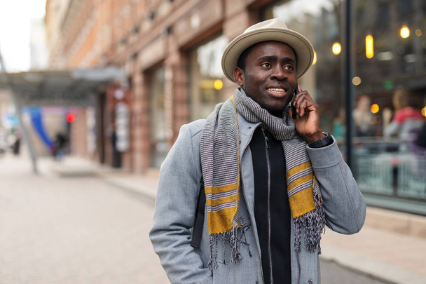 Happy african american man talks with his friend by smartphone walking in city - Fotó, kép